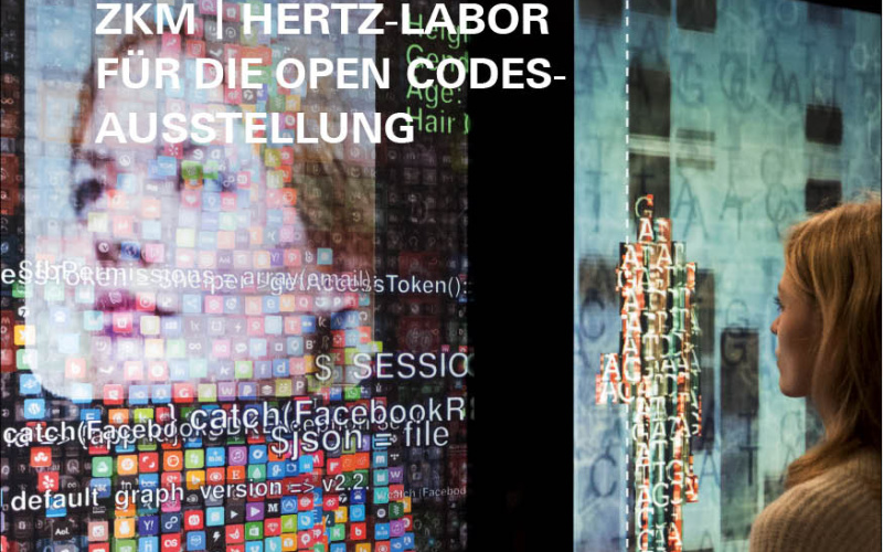 A woman stands in front of the artwork YOU:R:CODE that consists of large screens